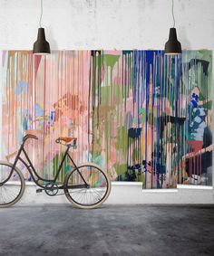 a bike is parked in front of an abstract painting on the wall and two lamps are hanging above it