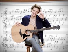 a man sitting on top of a wooden chair holding a guitar in front of musical notes