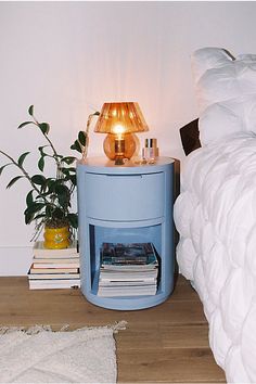 a nightstand with a lamp on top of it next to a bed and a potted plant