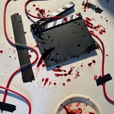 a white table topped with red and black wires and blood on the floor next to a movie clapper