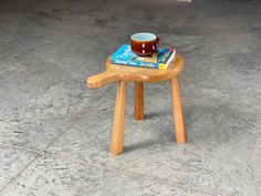 a small wooden stool with a book on it and a coffee mug sitting on top