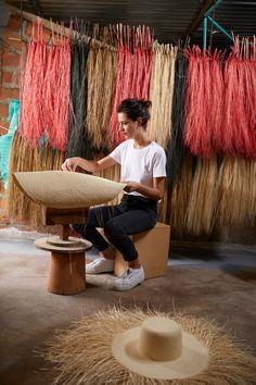 a woman sitting on a bench in front of some straws and weaving material hanging from the ceiling