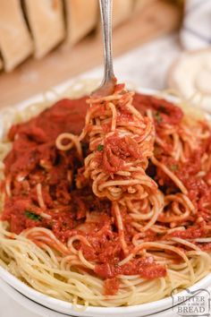 a fork full of spaghetti with sauce in a white bowl on top of a table