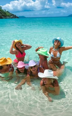 several women in bikinis and hats standing in the water