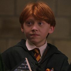 a young boy with red hair wearing a harry potter outfit and holding a wand in his hand