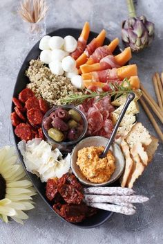 a platter filled with meats, vegetables and crackers next to a sunflower