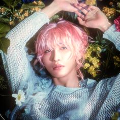 a woman with pink hair and blue eyes posing in front of flowers holding her hands up to her head