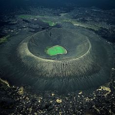 an aerial view of a green crater in the middle of some water with rocks around it