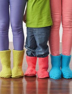 three children standing next to each other wearing colorful crocheted boots and leg warmers