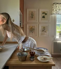 a woman leaning over a kitchen counter with food on the counter and bowls in front of her