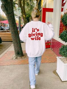 a woman is walking down the sidewalk wearing a sweatshirt that says it's giving wife