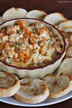 a white plate topped with crackers and a bowl filled with dip surrounded by bread