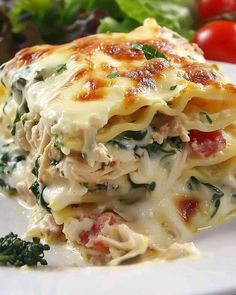 a white plate topped with lasagna covered in chicken and cheese next to vegetables