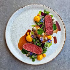 a white plate topped with meat and vegetables on top of a gray countertop next to a bottle of wine