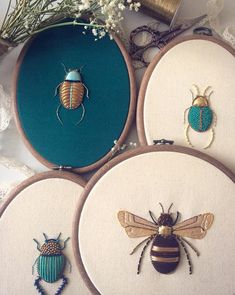 four embroideryed bugs and one bug on white fabric with flowers in the back ground