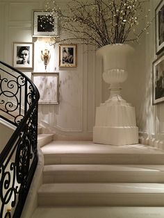 a white staircase with pictures on the wall and flowers in a vase next to it