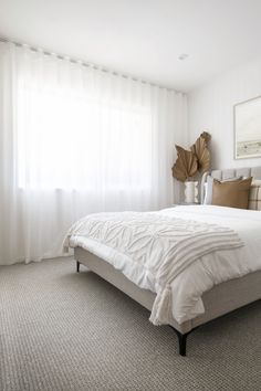 a white bed sitting in a bedroom next to a window with sheer curtains on it