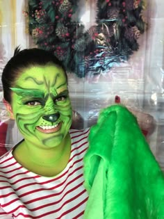 a young boy with green face paint holding a stuffed animal in front of christmas wreaths