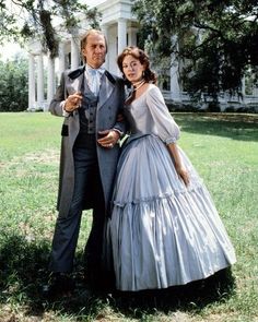 a man and woman dressed in period clothing standing next to each other on the grass