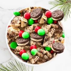 a bowl filled with cookies and candy on top of a white table next to pine branches