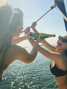 two beautiful women on a boat with bottles in their hands and one holding onto the side of the boat