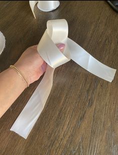 a woman's hand holding a white ribbon on top of a wooden table