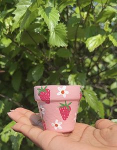 a pink cup with strawberries on it is held in front of some green leaves