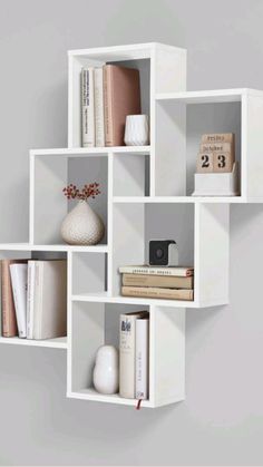 a white shelf with books and vases on it's sides, against a gray wall