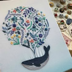 an embroidered whale with flowers and leaves on it's back, next to buttons