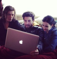 three people sitting on a couch looking at an apple laptop