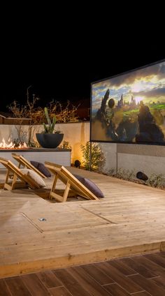 a wooden deck with two lounge chairs and a large screen on the wall behind it