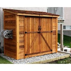 a wooden storage shed with sliding doors on the front door and side wall, next to a lawn