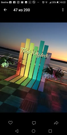 a colorful chair sitting on top of a wooden deck next to the ocean at sunset