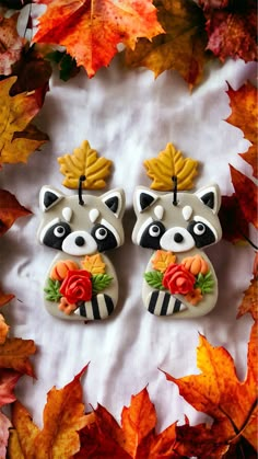 two raccoon figurines sitting on top of some leaves and one is holding a flower