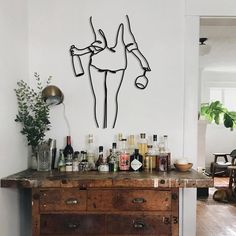 a wooden table topped with lots of bottles and glasses next to a painting on the wall