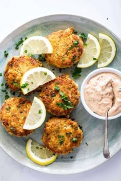 crab cakes with tartar sauce and lemon wedges on a plate next to a spoon