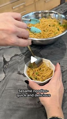 two hands are scooping noodles out of a pan