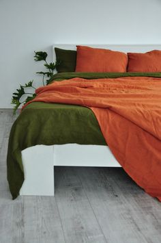 a bed with orange and green sheets in a white room next to a potted plant