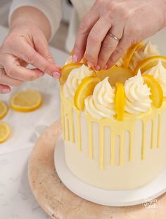 two people are decorating a cake with lemons and icing on the table