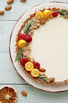 a white plate topped with a cake covered in fruit and nuts next to sliced oranges