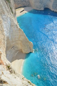 the water is blue and clear at the bottom of the cliff face, with cliffs in the background