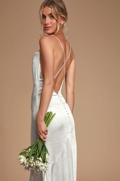 a woman in a white dress is holding a bouquet and looking back at the camera