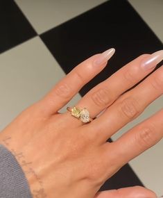 a woman's hand with a diamond ring on top of her finger and a black and white checkered floor in the background