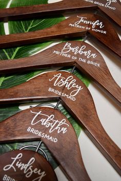 six wooden hangers with names on them sitting on a table next to green leaves