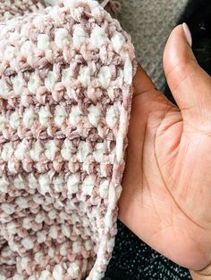 a hand is holding up a crocheted piece of cloth that looks like a blanket