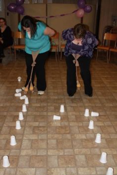 two women are playing with white cups on the floor and balloons flying in the air