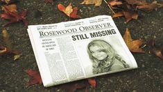 a newspaper laying on the ground with autumn leaves around it and an image of a woman's face