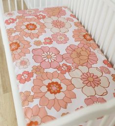 a white crib with an orange and pink flowered sheet on it's side