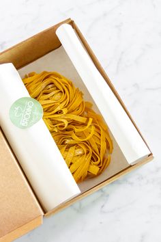 an open box with pasta in it on a marble counter top next to a roll of white paper