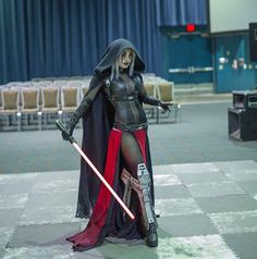 a woman dressed up as darth vader in a convention hall with two swords